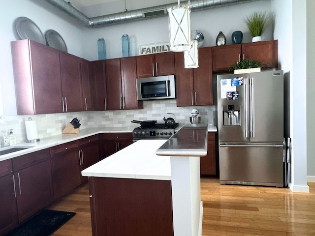 kitchen featuring a center island, stainless steel appliances, hanging light fixtures, light hardwood / wood-style flooring, and backsplash