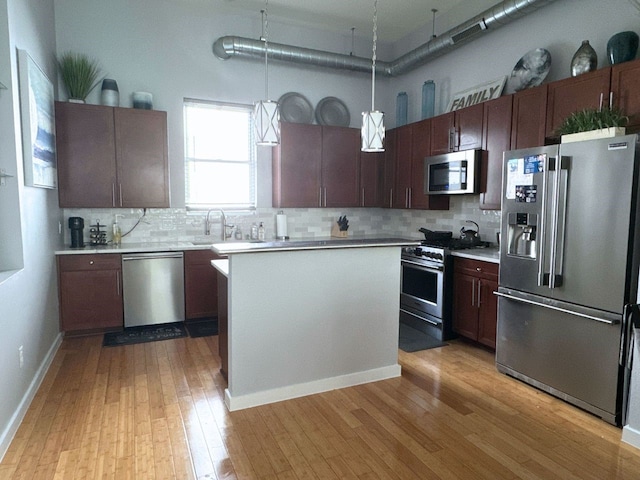 kitchen featuring decorative backsplash, hanging light fixtures, stainless steel appliances, and light hardwood / wood-style flooring