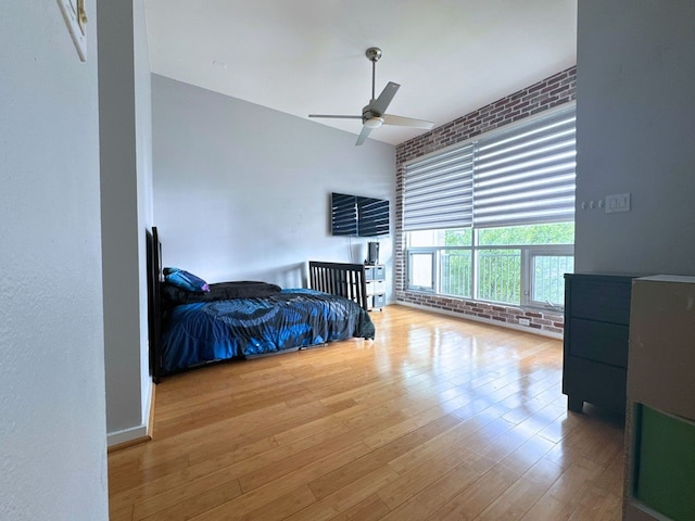 bedroom featuring ceiling fan, hardwood / wood-style flooring, and brick wall