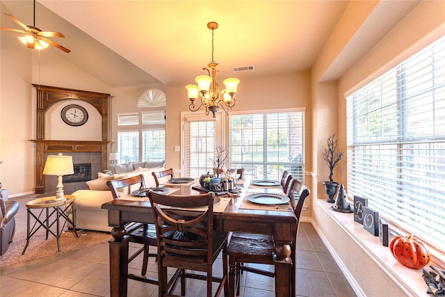 tiled dining space with a fireplace, ceiling fan with notable chandelier, and vaulted ceiling