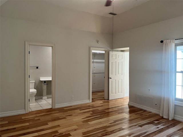 unfurnished bedroom featuring light hardwood / wood-style flooring, ensuite bathroom, a walk in closet, and ceiling fan