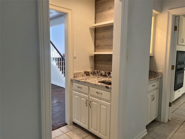 kitchen with oven, white cabinets, light stone countertops, and light tile patterned floors