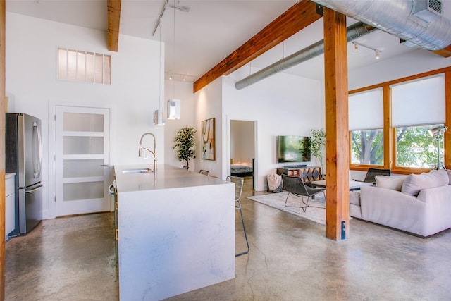 kitchen with beam ceiling, sink, stainless steel fridge, pendant lighting, and a kitchen island with sink