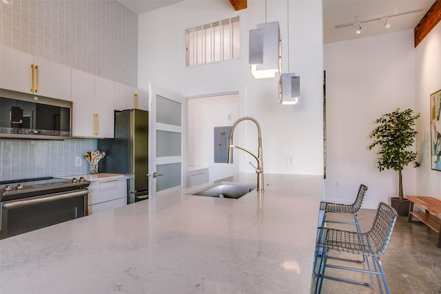 kitchen featuring sink, tasteful backsplash, light stone counters, white cabinets, and appliances with stainless steel finishes