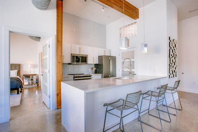 kitchen with a high ceiling, white cabinets, hanging light fixtures, appliances with stainless steel finishes, and beam ceiling