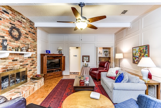 living room with ceiling fan, beam ceiling, light parquet flooring, a brick fireplace, and a textured ceiling