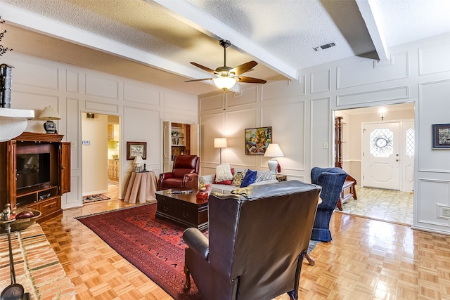 living room with ceiling fan, a textured ceiling, beam ceiling, and light parquet flooring