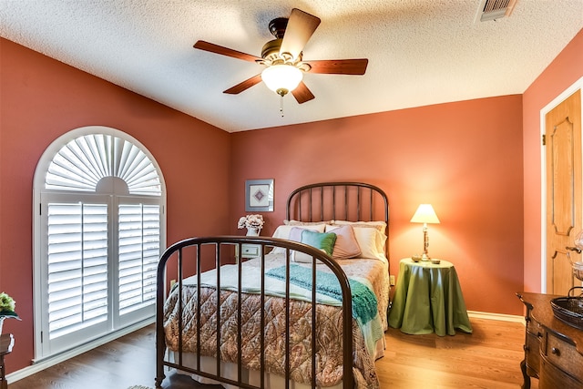 bedroom featuring ceiling fan, a textured ceiling, hardwood / wood-style floors, and multiple windows