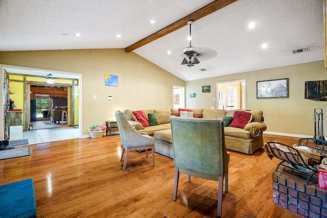 living room with light wood-type flooring, vaulted ceiling with beams, and a textured ceiling