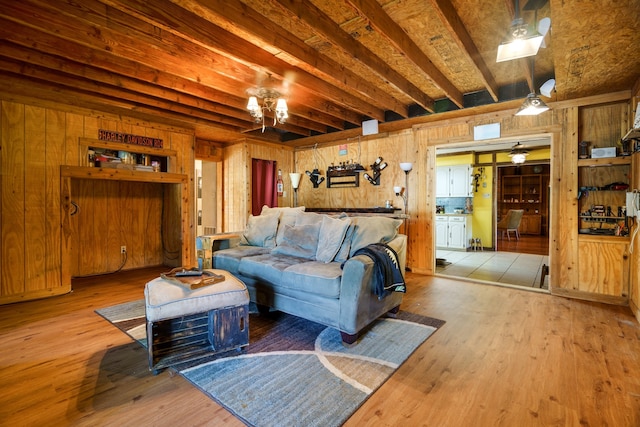 living room with ceiling fan, beamed ceiling, wooden walls, and hardwood / wood-style floors