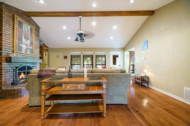 living room with a brick fireplace, lofted ceiling with beams, ceiling fan, hardwood / wood-style flooring, and a textured ceiling