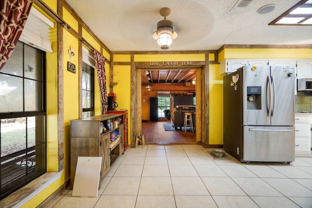 kitchen with crown molding, stainless steel refrigerator with ice dispenser, a textured ceiling, and white cabinetry