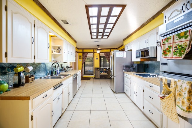 kitchen featuring tasteful backsplash, sink, appliances with stainless steel finishes, light tile patterned floors, and white cabinetry