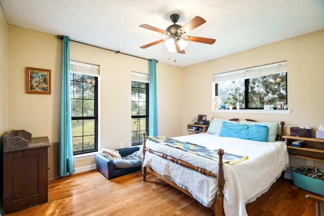 bedroom with light wood-type flooring, multiple windows, ceiling fan, and a textured ceiling