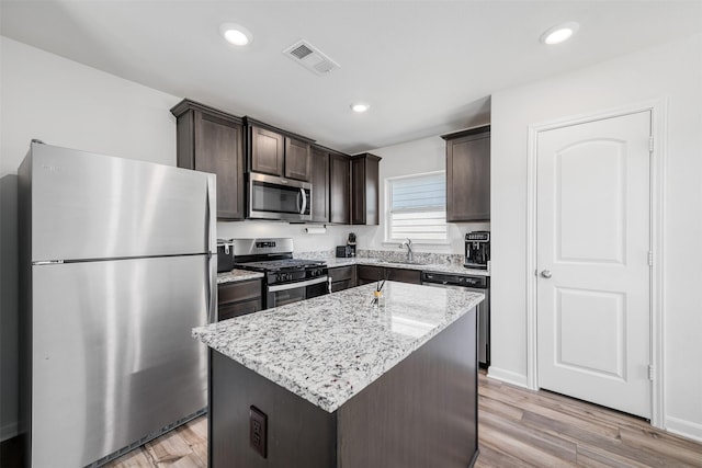 kitchen with appliances with stainless steel finishes, sink, a center island, light stone counters, and light wood-type flooring