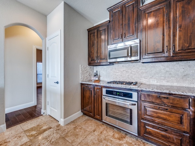 kitchen featuring decorative backsplash, appliances with stainless steel finishes, light stone counters, and dark brown cabinets