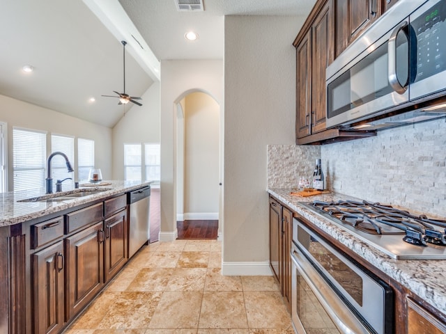 kitchen with lofted ceiling, decorative backsplash, light stone counters, appliances with stainless steel finishes, and sink