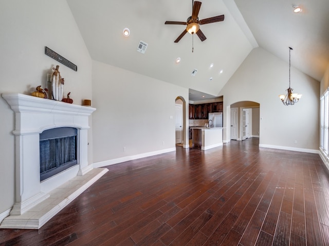 unfurnished living room with dark wood-type flooring, high vaulted ceiling, and ceiling fan with notable chandelier