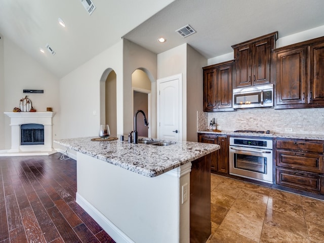 kitchen featuring dark hardwood / wood-style flooring, appliances with stainless steel finishes, a kitchen island with sink, vaulted ceiling, and sink