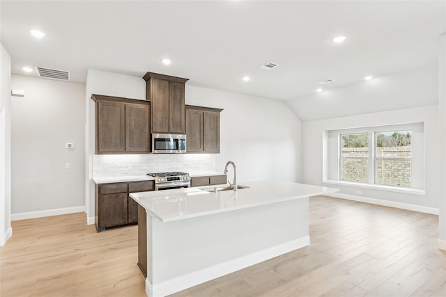 kitchen featuring sink, lofted ceiling, an island with sink, and appliances with stainless steel finishes