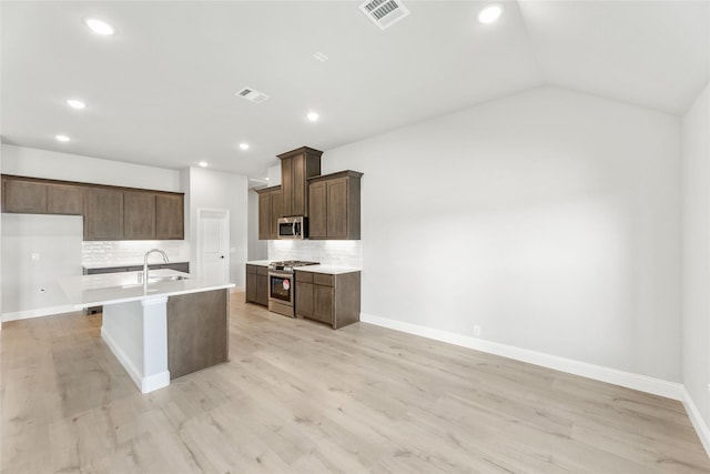 kitchen featuring vaulted ceiling, stainless steel appliances, decorative backsplash, a kitchen island with sink, and sink