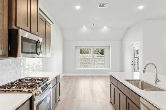 kitchen with appliances with stainless steel finishes, sink, a kitchen island with sink, and light wood-type flooring