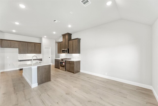 kitchen with stainless steel appliances, sink, a center island with sink, and light hardwood / wood-style flooring