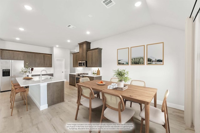 kitchen with vaulted ceiling, an island with sink, light hardwood / wood-style floors, appliances with stainless steel finishes, and sink