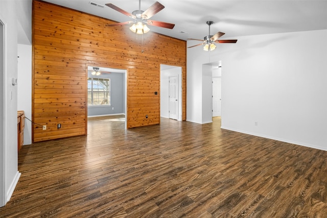 unfurnished room with baseboards, visible vents, dark wood-style floors, wood walls, and high vaulted ceiling