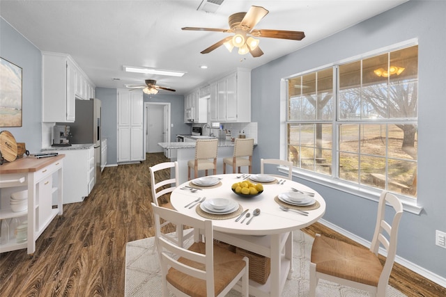 dining room with a ceiling fan, plenty of natural light, baseboards, and dark wood-type flooring