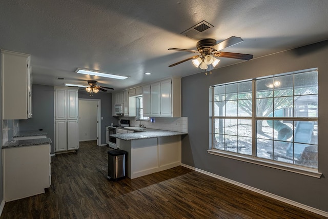 kitchen with a skylight, white cabinetry, dark hardwood / wood-style floors, and white appliances