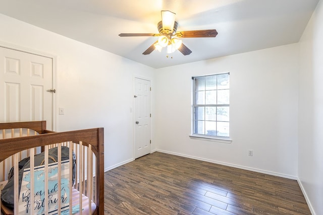 unfurnished bedroom featuring ceiling fan, dark wood-type flooring, and a nursery area