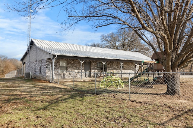 exterior space with metal roof, a playground, central air condition unit, brick siding, and fence