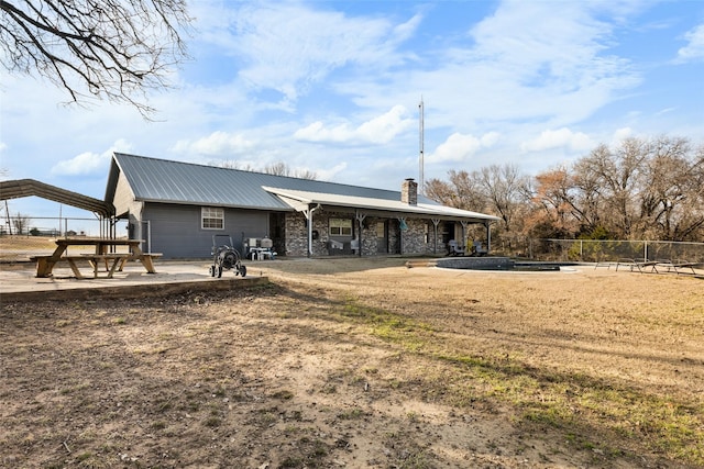 back of property with a chimney, a detached carport, a patio area, metal roof, and fence