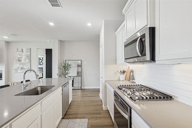 kitchen with dark wood-type flooring, stainless steel appliances, backsplash, sink, and white cabinetry