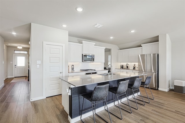 kitchen with appliances with stainless steel finishes, white cabinets, a kitchen island with sink, and light wood-type flooring