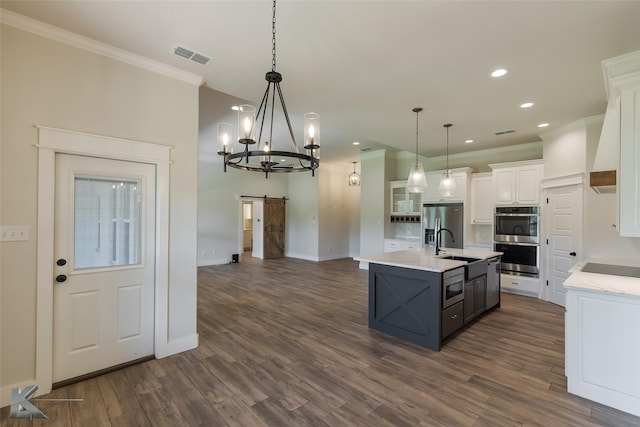 kitchen with a center island with sink, decorative light fixtures, a barn door, and white cabinets