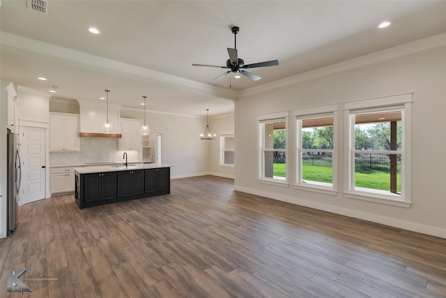 kitchen featuring crown molding, sink, a center island with sink, white cabinetry, and stainless steel refrigerator