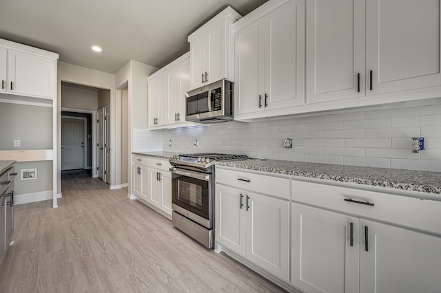 kitchen with light hardwood / wood-style floors, white cabinets, backsplash, light stone countertops, and appliances with stainless steel finishes