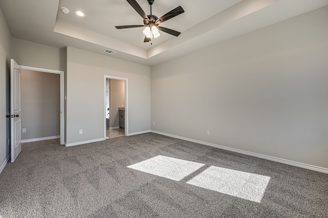 unfurnished bedroom featuring ensuite bath, carpet floors, ceiling fan, and a raised ceiling