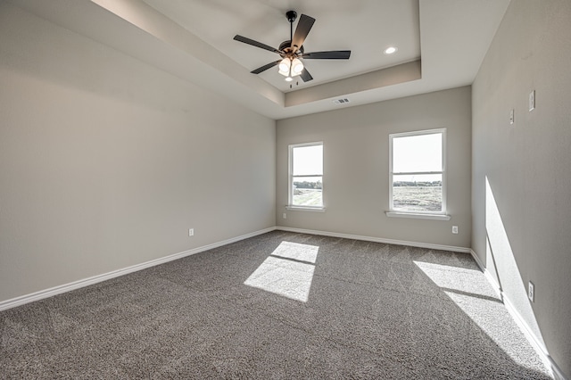 carpeted spare room featuring a tray ceiling and ceiling fan