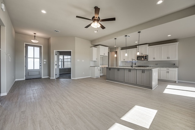 kitchen with a center island with sink, white cabinets, tasteful backsplash, light wood-type flooring, and decorative light fixtures