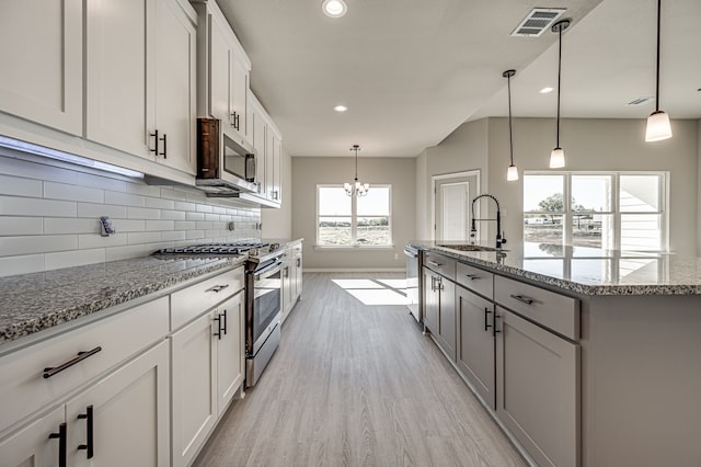 kitchen with stainless steel appliances, light hardwood / wood-style floors, sink, a kitchen island with sink, and pendant lighting