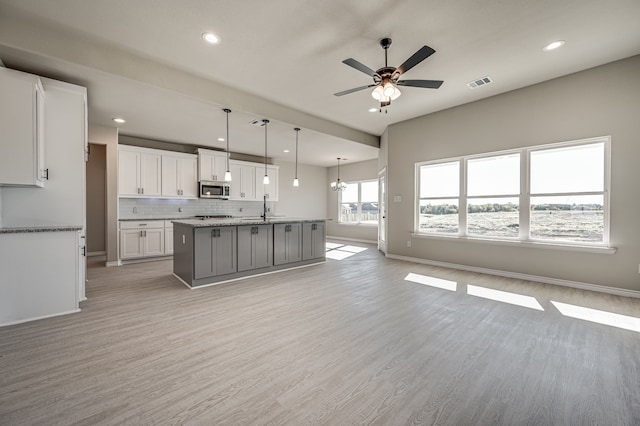 kitchen with light hardwood / wood-style floors, white cabinets, hanging light fixtures, sink, and a kitchen island with sink