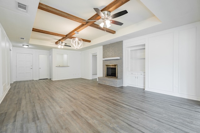 unfurnished living room with light wood-type flooring, a fireplace, ceiling fan, and a raised ceiling