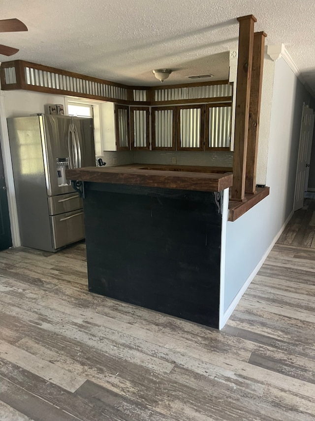 kitchen with a textured ceiling, crown molding, wood-type flooring, and stainless steel refrigerator with ice dispenser