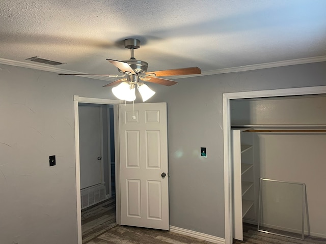 unfurnished bedroom with ceiling fan, a closet, dark hardwood / wood-style floors, ornamental molding, and a textured ceiling