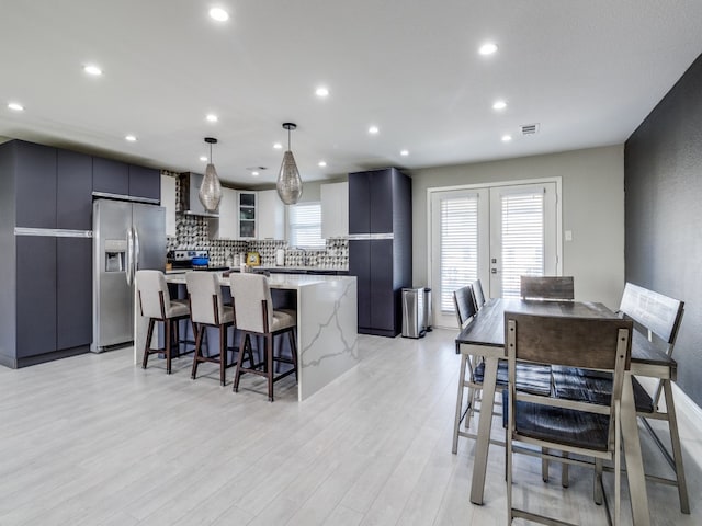 kitchen with stainless steel appliances, light hardwood / wood-style floors, hanging light fixtures, a kitchen island, and wall chimney range hood