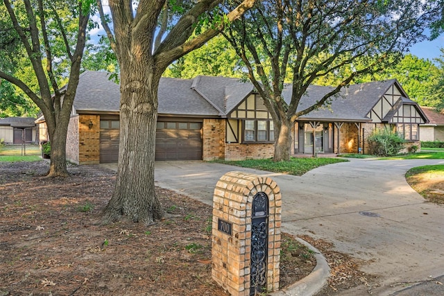 english style home with a garage, brick siding, concrete driveway, and a shingled roof