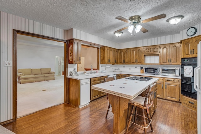 kitchen featuring wood-type flooring, sink, a kitchen island, black appliances, and a breakfast bar area